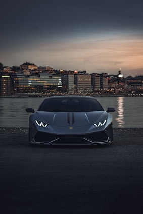 A sleek luxury sports car parked in front of a modern cityscape at sunset.