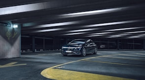A sleek black car being carefully parked by triparking staff in a secure parking area with bright, professional lighting.