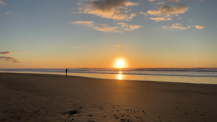 A serene beach sunset with a lone traveler gazing at the horizon, embodying wanderlust and calm.