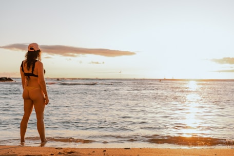 A woman wearing a stylish protective swimsuit standing by the ocean shore at sunset.