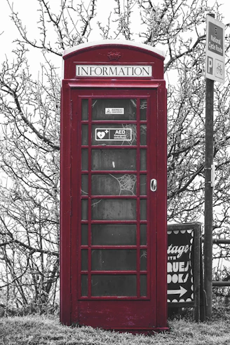 a red telephone booth sitting next to a street sign