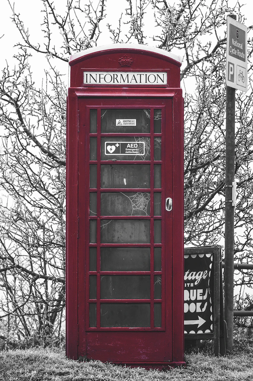 a red telephone booth sitting next to a street sign