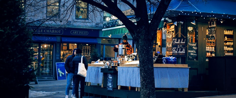 a man standing outside of a store next to a tree