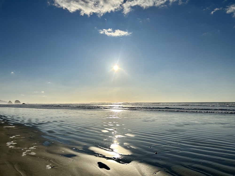 the sun is shining over the water on the beach