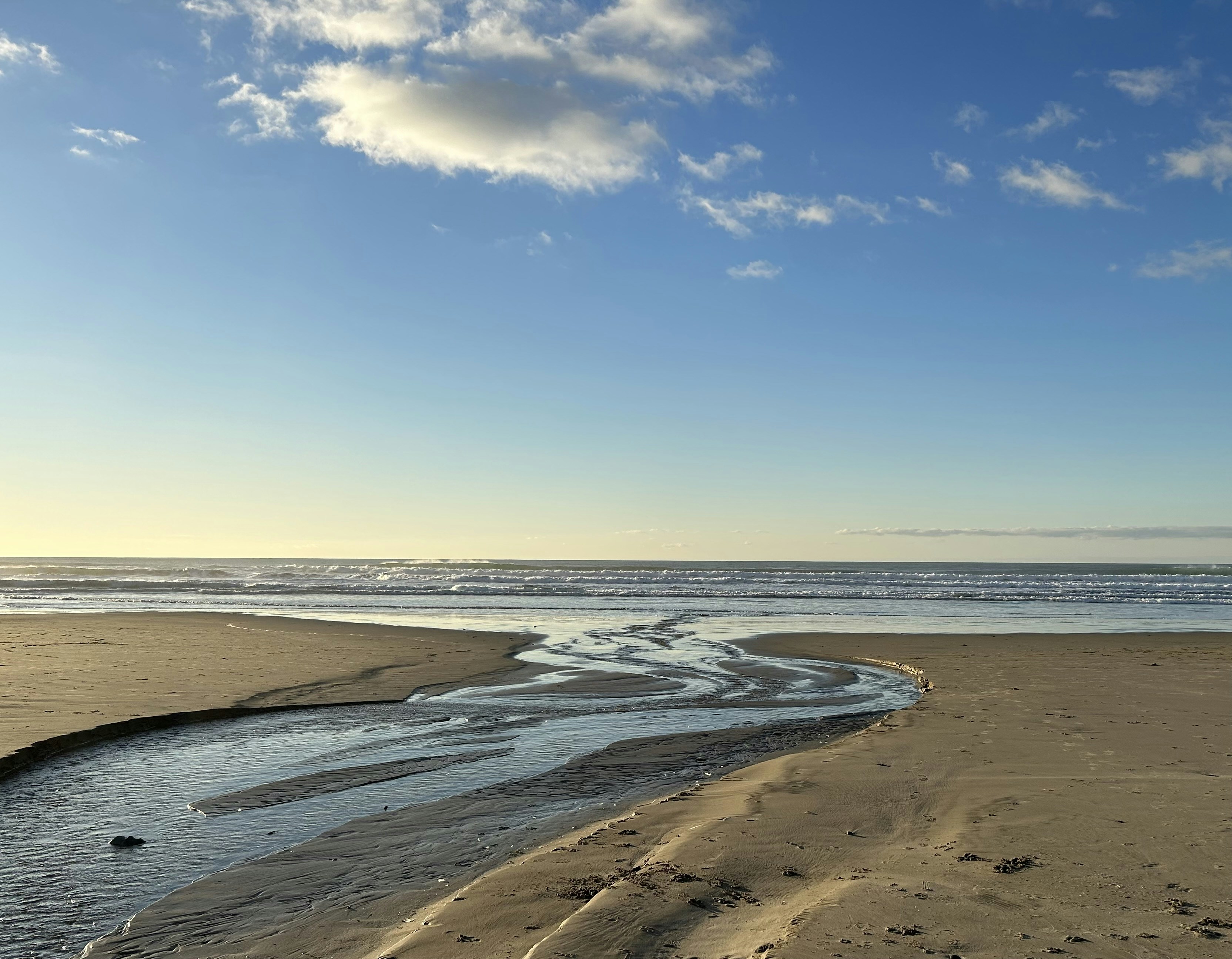 a sandy beach next to the ocean under a blue sky
