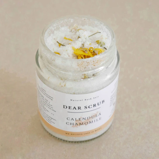 Close-up of hand-poured healing balm jars with natural ingredients like calendula and lavender arranged on a linen cloth.