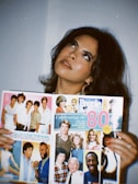 A person with dark hair and makeup is holding a magazine featuring a collage of people and articles titled 'Celebrating the '80s'. The magazine includes various images and colors, which evoke a retro theme.