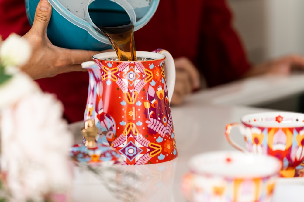 a person pouring tea into a colorful teapot