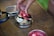 A close-up view of a person picking dried fruit from a small, open metal tin containing a mix of snacks including dried fruits and pretzels on a wooden table.