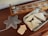 A wooden table holds a decorative object shaped like a snowflake next to a wooden board game with metal sliders. A metallic tray contains several smooth, cream-colored geometric shapes.