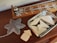 A wooden table holds a decorative object shaped like a snowflake next to a wooden board game with metal sliders. A metallic tray contains several smooth, cream-colored geometric shapes.