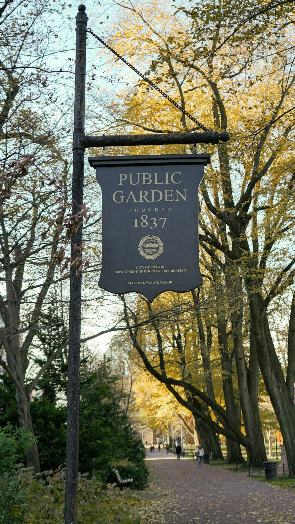 a public garden sign hanging from a metal pole