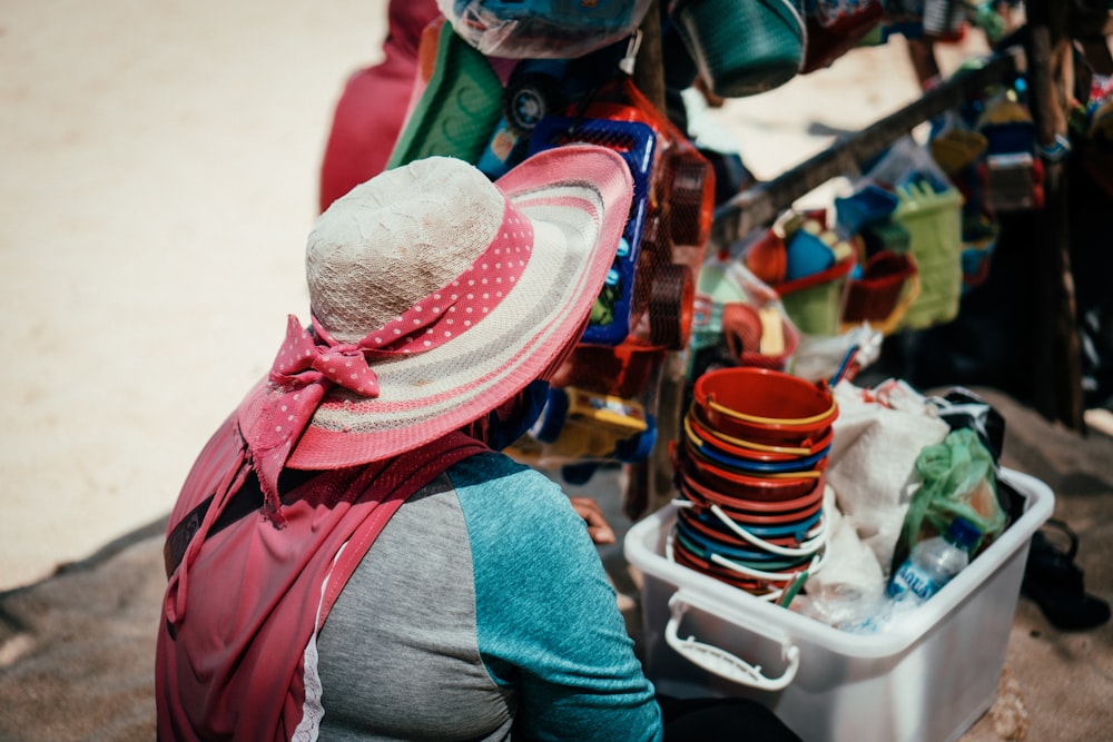 a woman sitting on the ground next to a pile of hats