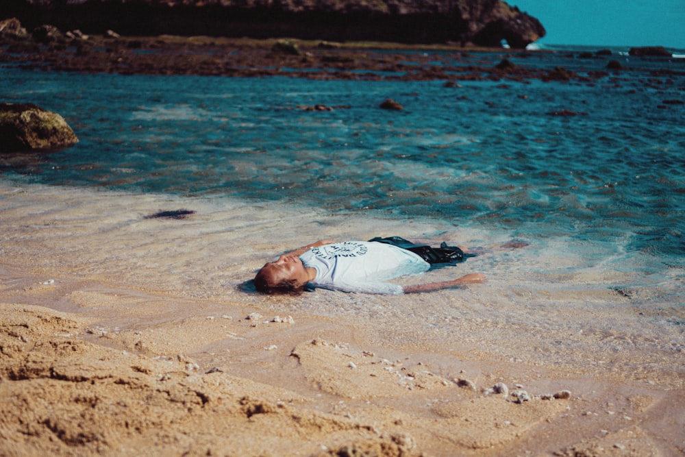 a man laying on top of a sandy beach next to the ocean