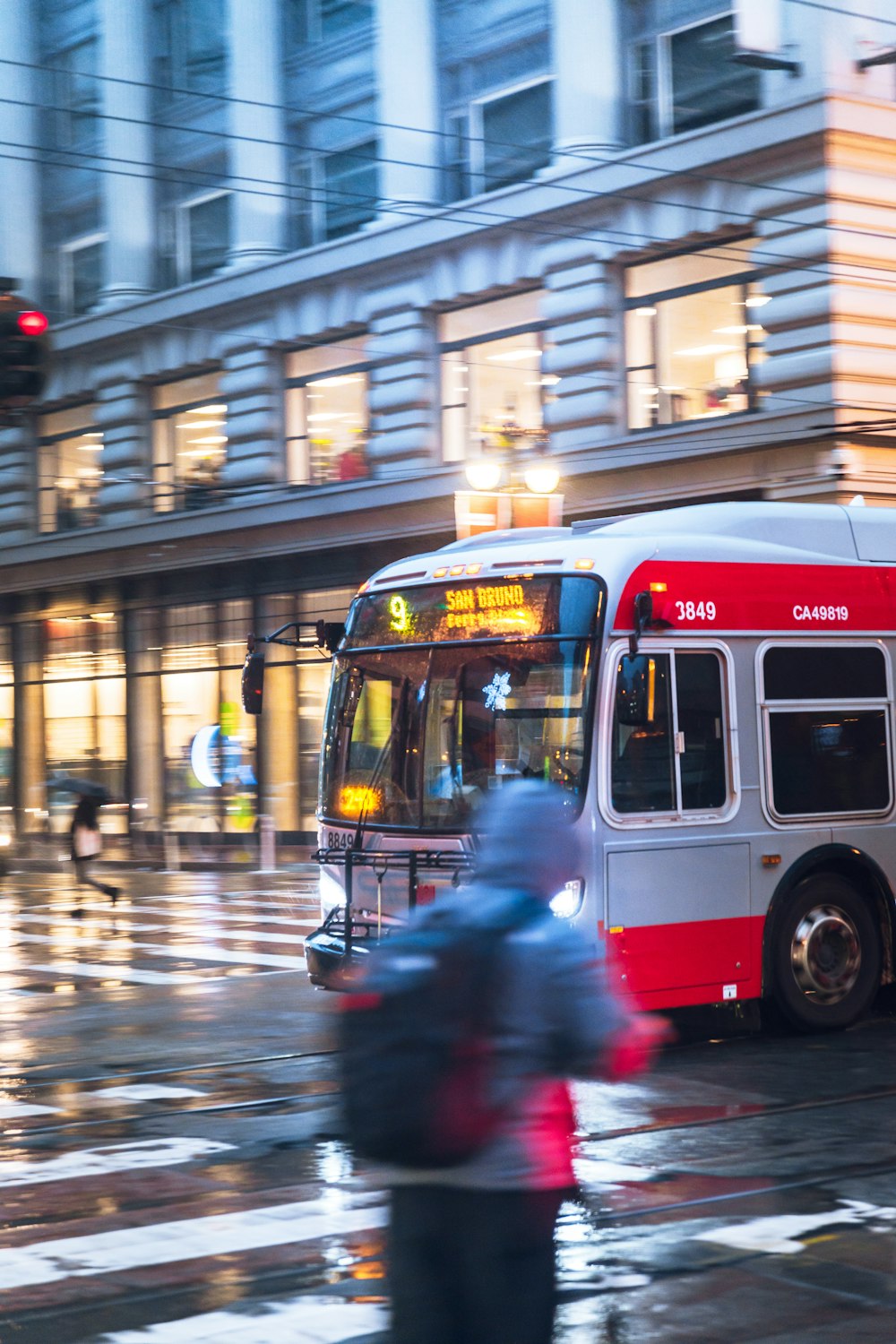 a red and white bus driving down a street next to a tall building