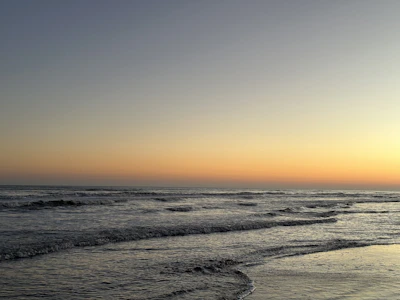 A serene beach scene at dusk with soft waves and a warm sky.
