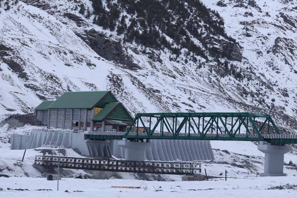 a green bridge over a river next to a snow covered mountain