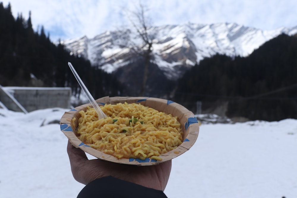 a person holding a bowl of noodles in the snow