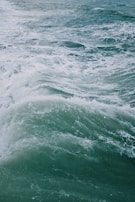 Large ocean waves with foamy white crests rolling across the sea. The water is a deep greenish-blue, indicating depth and strength.