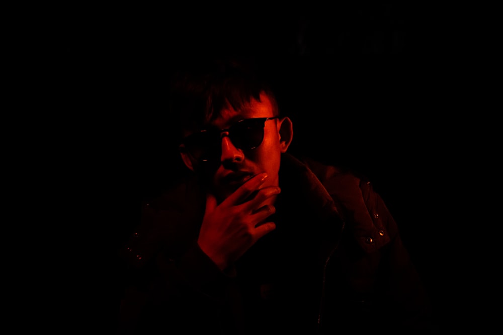선글라스를 쓴 남자가 어둠 속에서 담배를 피우고 있다