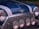 A close-up of a classic car's front, exhibiting a glossy blue paint with white racing stripes. There are four circular headlights and a chrome grille that enhance the vintage aesthetic. The manufacturer's emblem, which features wings and a red circle, is prominently displayed.