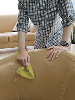 A professional cleaner using steam cleaning equipment on a sofa in a bright living room.