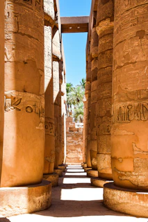 Golden sunlight filters through ancient columns at Luxor's Karnak Temple, casting long shadows on the sandstone.