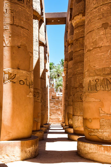 Golden sunlight filters through ancient columns at Luxor's Karnak Temple, casting long shadows on the sandstone.