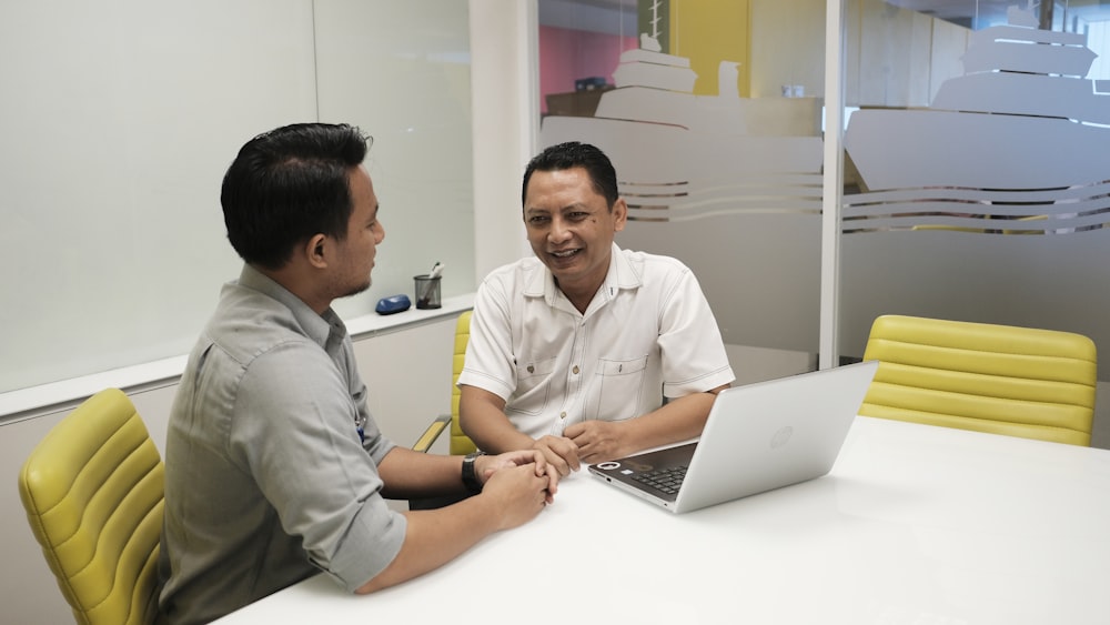 dois homens sentados em uma mesa com um laptop