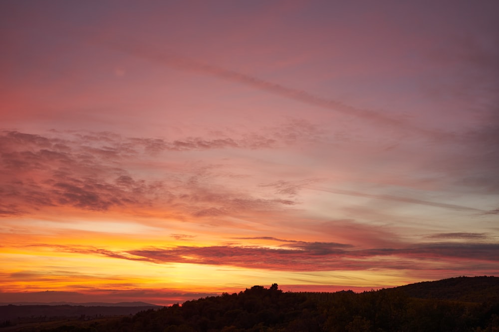 a sunset with clouds and trees in the foreground