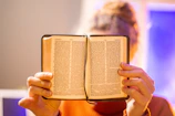 Close-up of hands holding an open Bible with soft morning light.