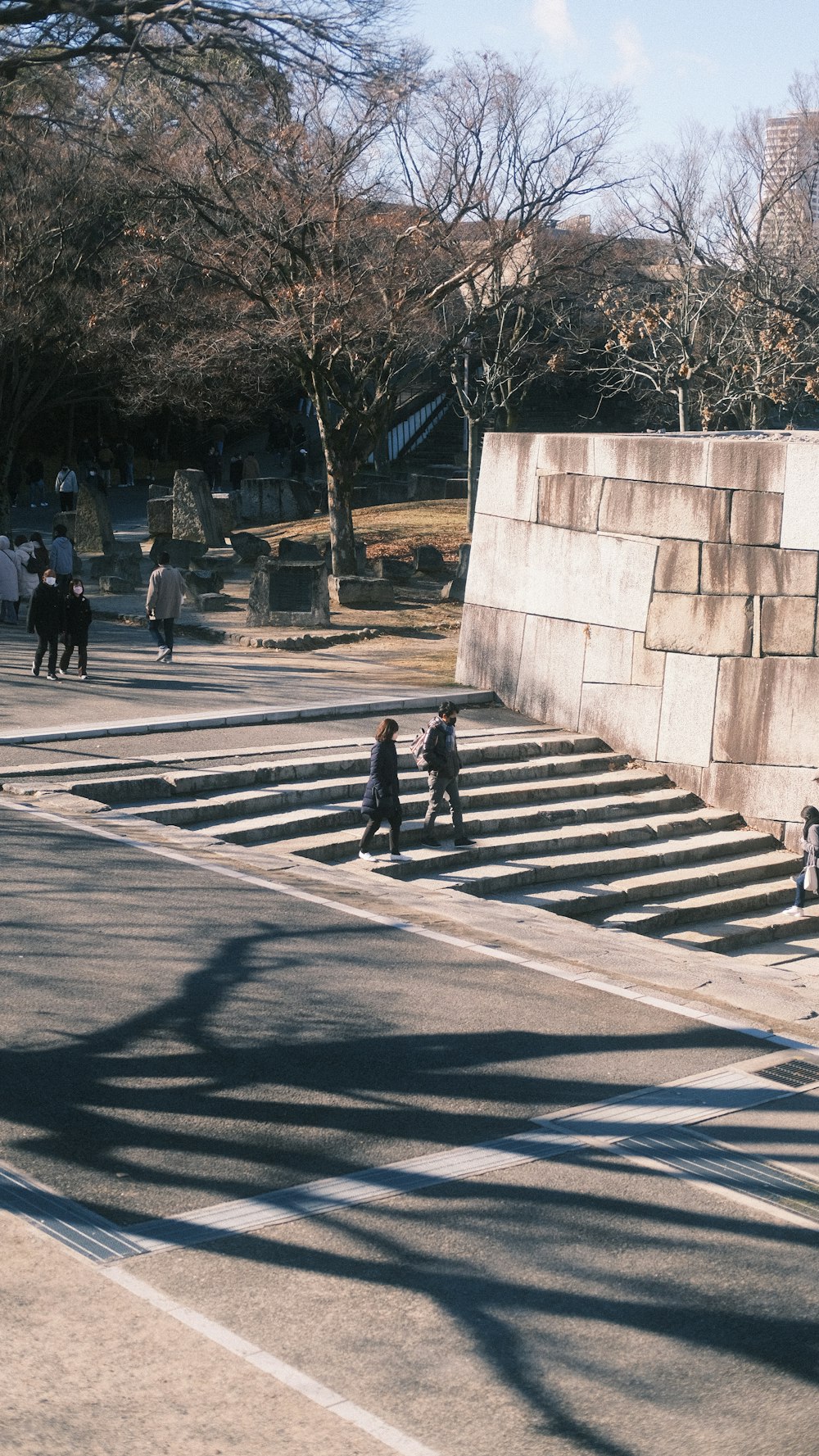 a group of people walking down a street next to a stone wall