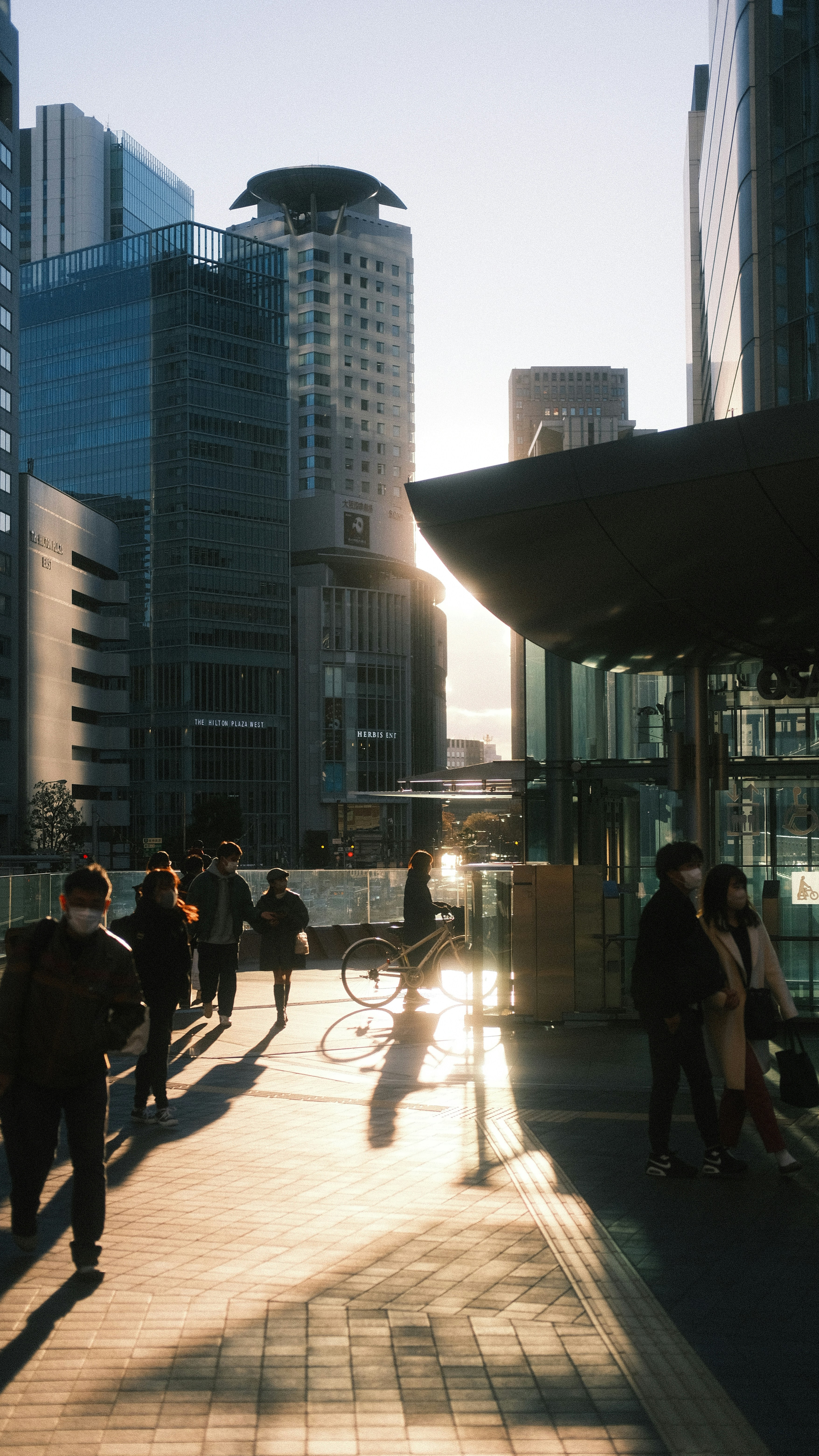 a group of people walking down a sidewalk next to tall buildings
