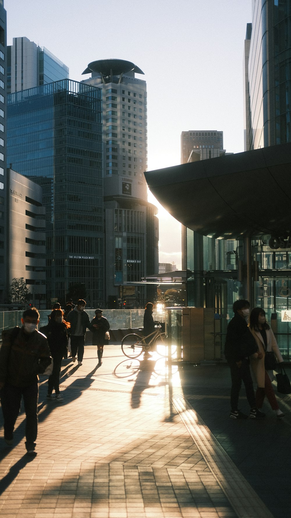 a group of people walking down a sidewalk next to tall buildings