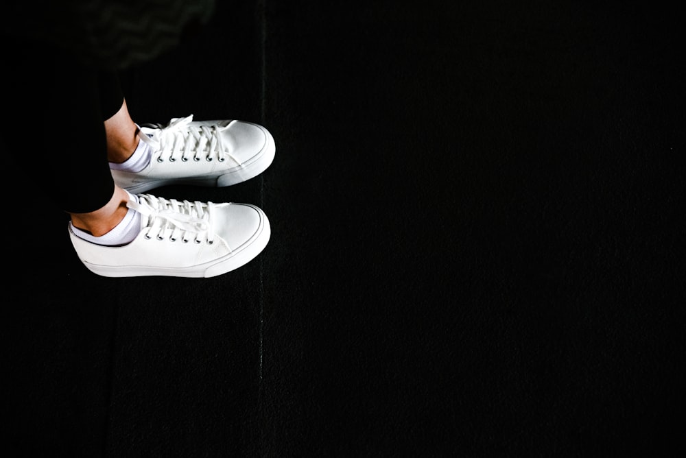 a person standing on a black surface wearing white sneakers