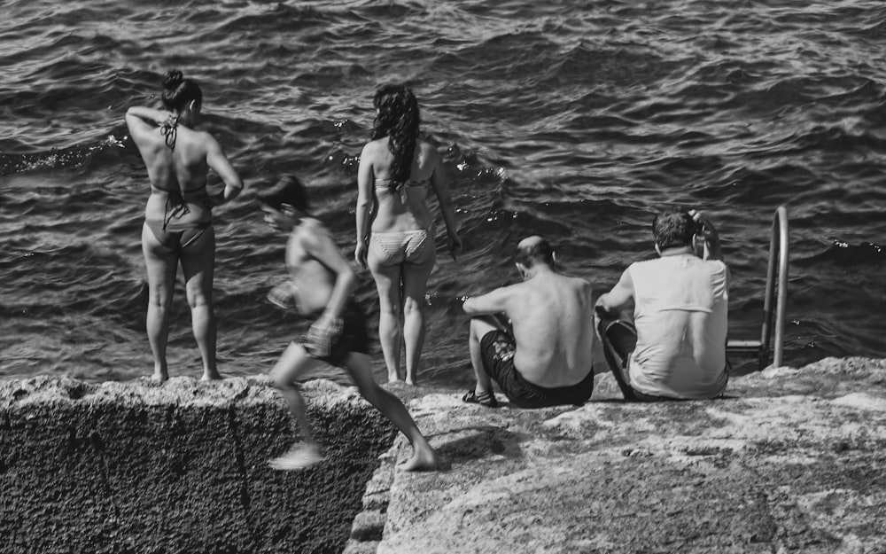 a group of people sitting on top of a rock next to the ocean