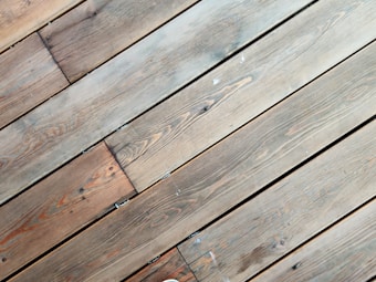 A series of parallel wooden planks with visible grain patterns and slight color variations. The wood appears aged and has a natural, rustic look with some knots and imperfections visible.