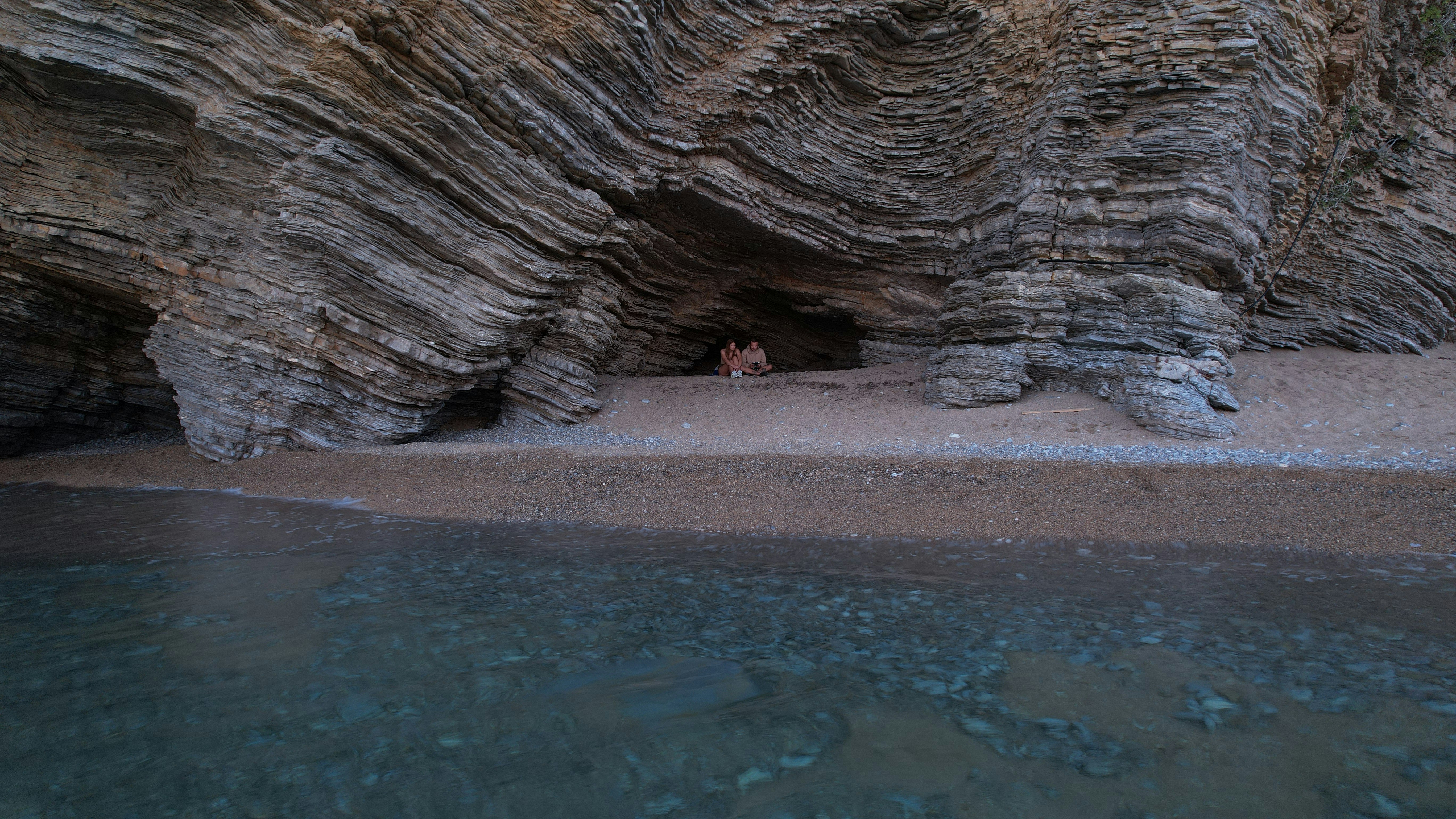 Two travelers exploring a natural cave located on a picturesque beach along the Montenegrin coast