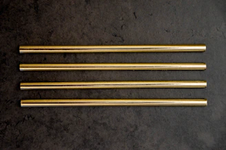 Set of golden drinking straws arranged artistically on a soft mint surface.