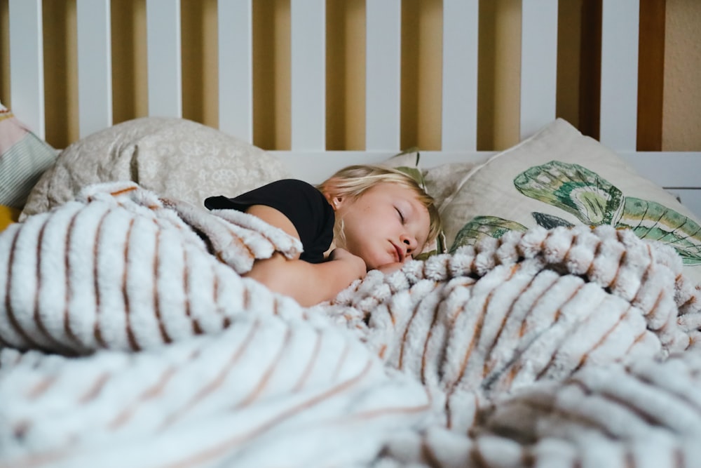 a little girl sleeping in a bed with a blanket