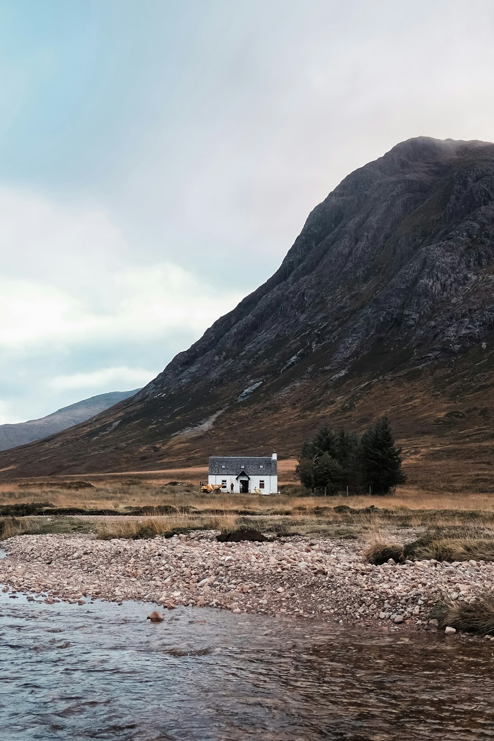 a house sitting on the side of a mountain next to a river