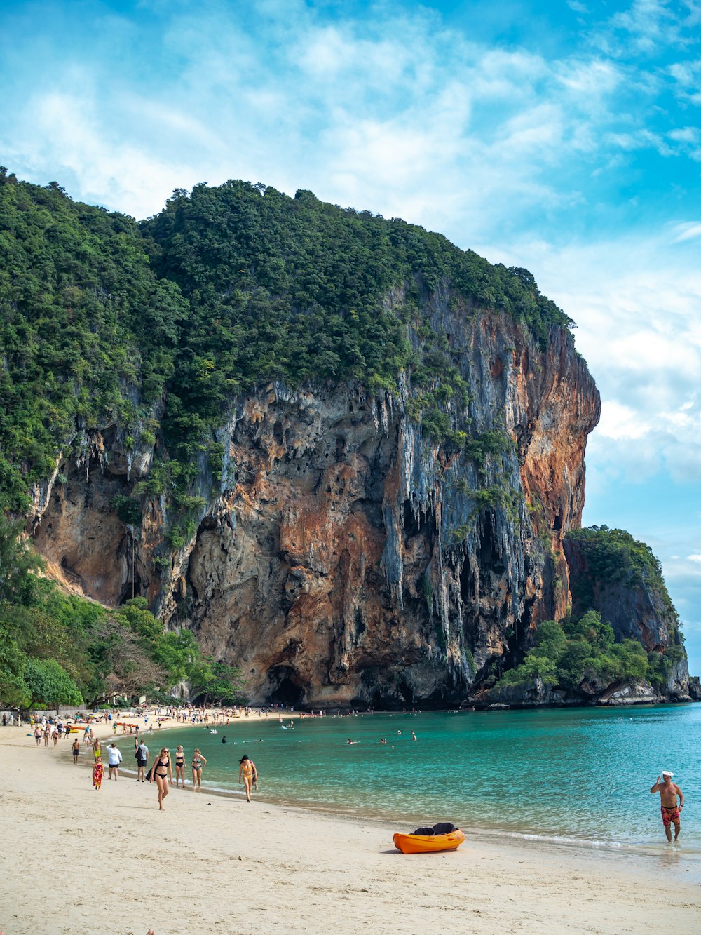 a group of people walking on a beach next to a mountain