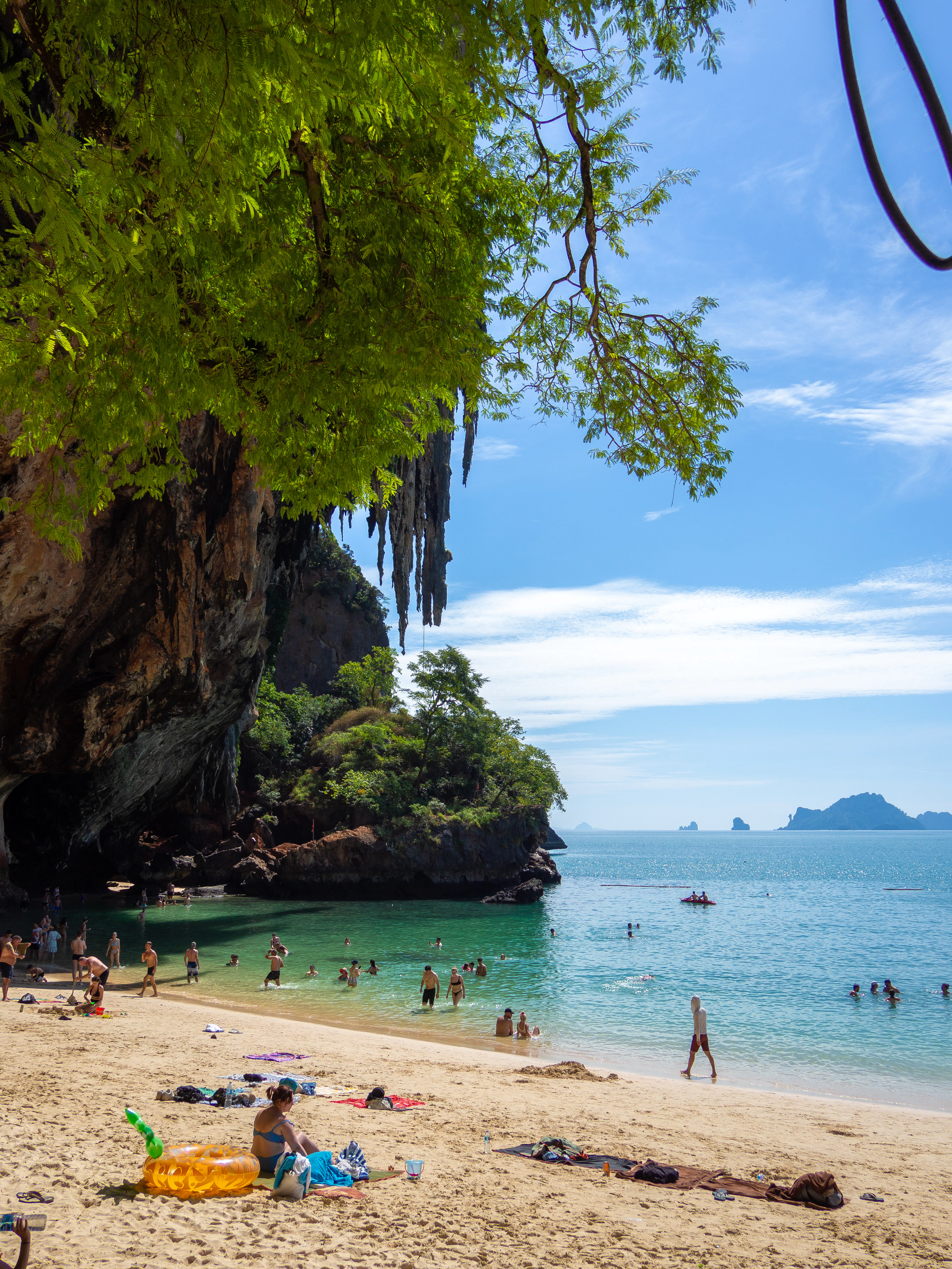 Swimmers in a turquoise lagoon framed by an overhanging cliff and cave at Phra Nang beach.
