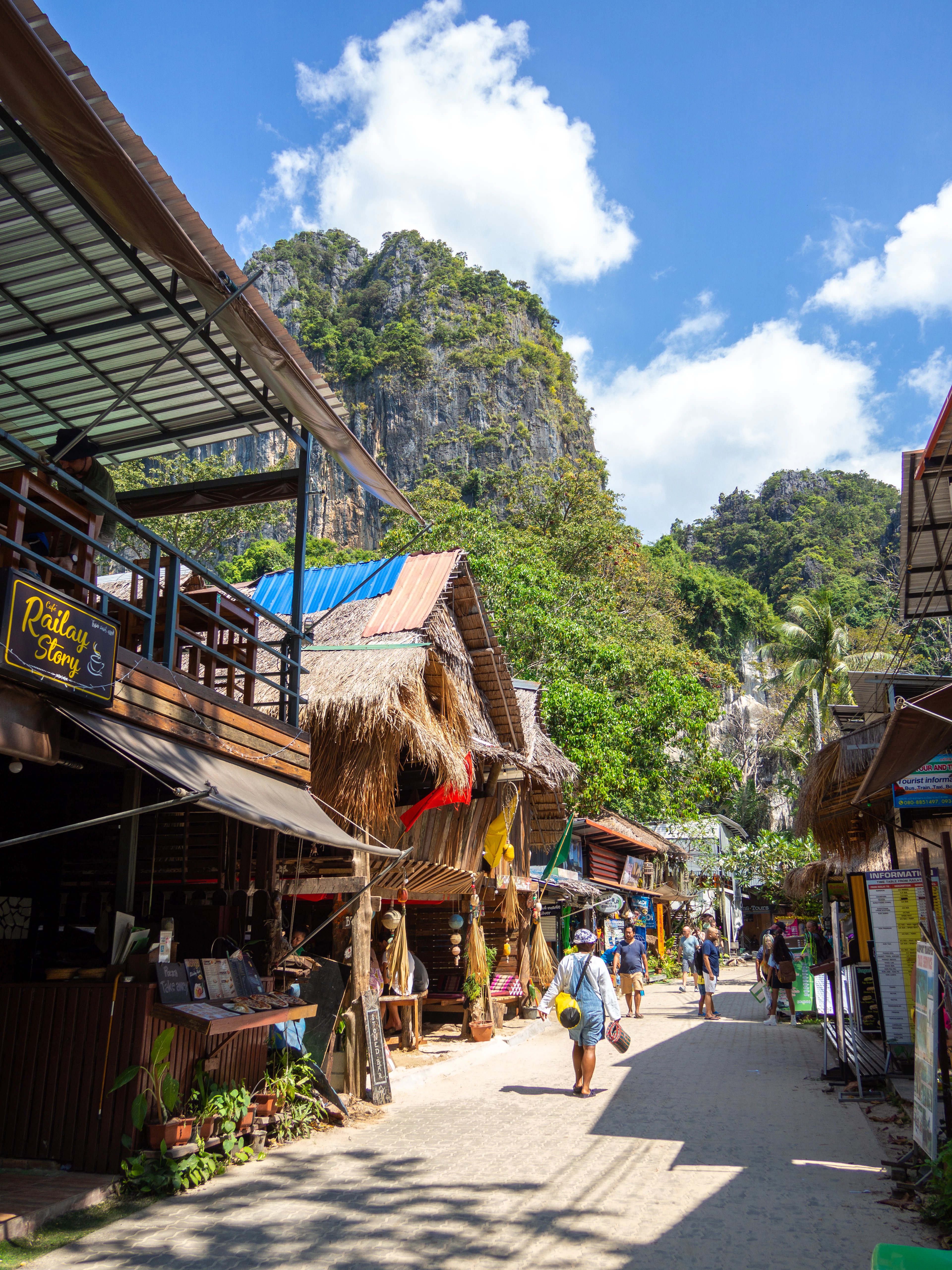 A limestone peak rises above Railay's sandy walking street lined with thatched-roof shops.