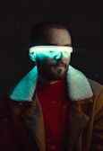 A person wearing a jacket with a fur collar and a red shirt. A futuristic visor emitting a glowing teal light covers the eyes, creating a cyberpunk aesthetic.