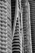 Tall, modern buildings with curved balconies and glass facades dominate the image. A construction scaffold is visible alongside one structure, suggesting ongoing development. The architectural design showcases sleek and futuristic aesthetics.