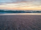 A tranquil scene of turquoise waves gently touching the golden sand at sunset.