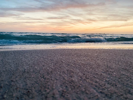 Sunset over a sandy Andalusian beach with gentle waves and a hint of orange sky.