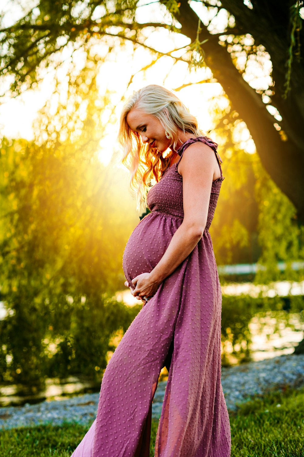 a pregnant woman in a purple dress standing in the grass