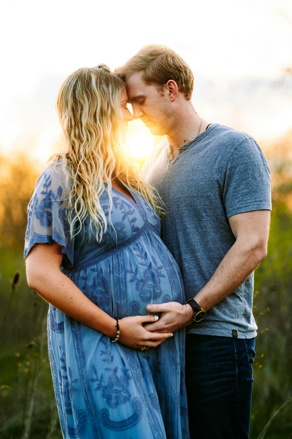 a pregnant couple kissing in a field at sunset
